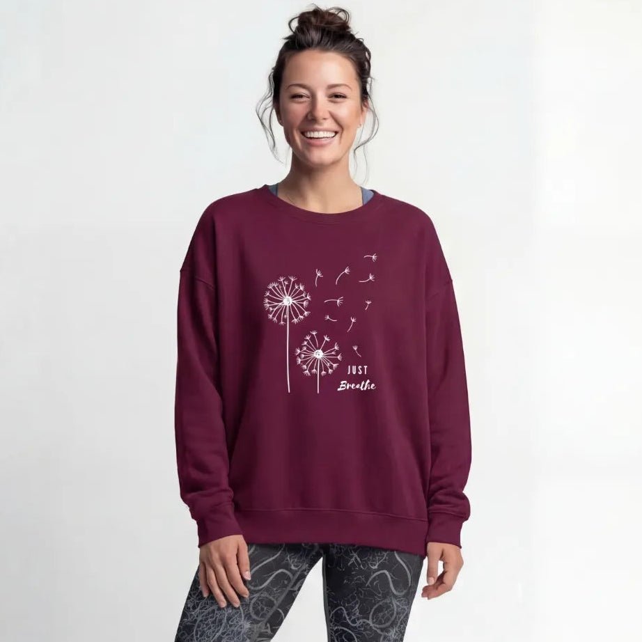 A person wearing a burgundy-coloured yoga sweater with the text “Just breathe”.